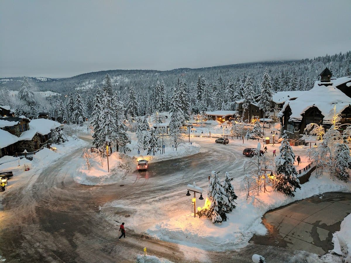 Village at Northstar under fresh snow at dusk, lit shopfronts around the village circle